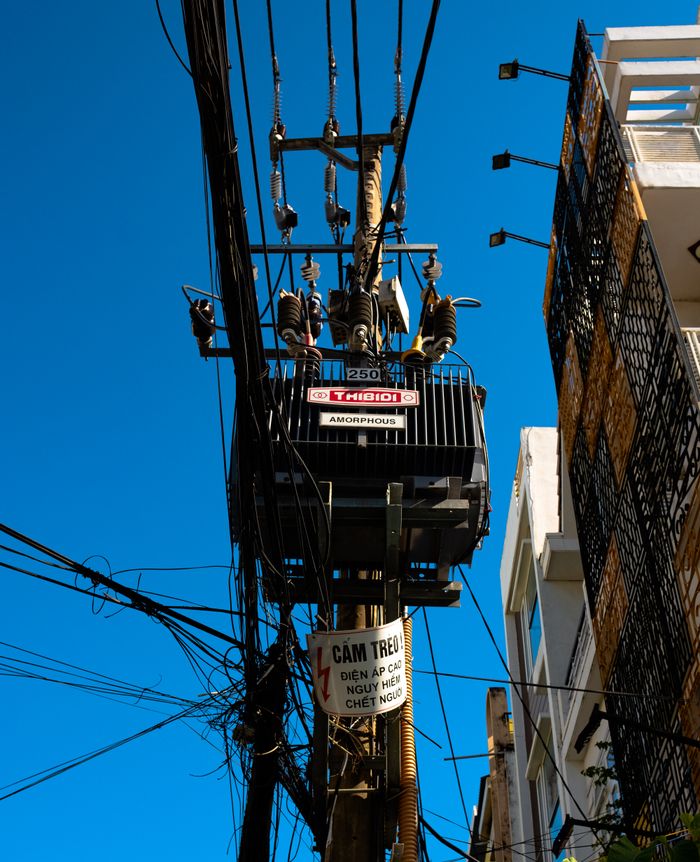 High-voltage transformer and wires against a clear blue sky in an urban setting.