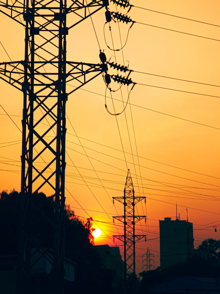 Contact Silhouettes of electric pylons against a sunset sky, highlighting industrial infrastructure.