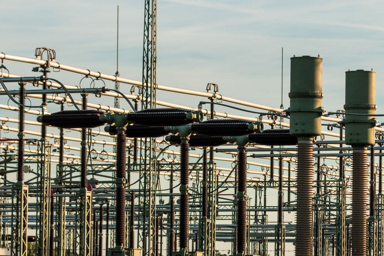 Services Detailed view of electrical substation with high voltage equipment and insulators against a clear sky.